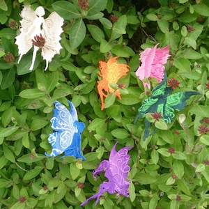 以下が含まれることがあります： 白、オレンジ、ピンク、青、緑、紫など、さまざまな色の刺繍された妖精のアップリケが6つあります。妖精はすべて、羽を広げて座った姿勢をしています。アップリケは緑の葉の背景にあります。