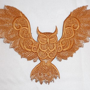 Könnte beinhalten: Gold gestickte Eulen-Applikation mit filigranen Details und einem ausgebreiteten Flügeldesign.