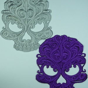 May include: Two embroidered skull patches, one silver and one purple. Both skulls have a detailed, ornate design with swirling patterns.