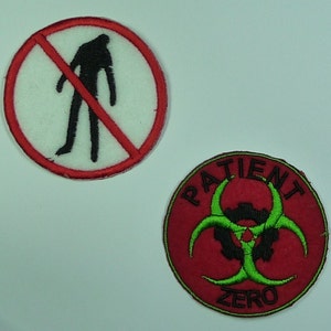 May include: Two embroidered patches. One is red with a white circle and a black silhouette of a person with a red line through it. The other is red with a green biohazard symbol and the text "PATIENT ZERO".
