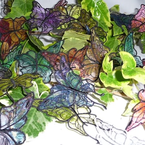May include: Assortment of colourful butterfly-shaped fabric appliques with iridescent glitter accents, arranged on a bed of green leaves.
