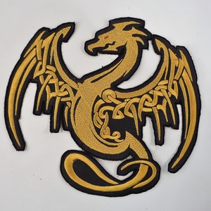 May include: Embroidered patch depicting a gold dragon with outstretched wings and Celtic knot patterns. The dragon has red eyes and a black border. Ideal for customising jackets, bags, or other fabric items.