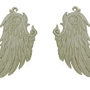 May include: Two light green embroidered angel wings with a detailed design. The wings are symmetrical and have a delicate, intricate pattern.