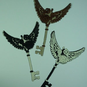 May include: Three embroidered iron-on patches in the shape of keys with wings. The keys are brown, black, and white with intricate details.
