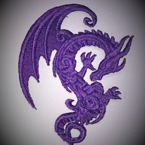 May include: Purple embroidered dragon design patch. The dragon is curled up with its wings spread out.
