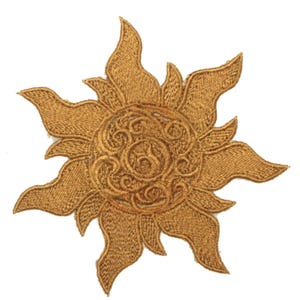 May include: A golden embroidered sun patch. The sun design has multiple pointed rays and a detailed, swirling pattern in the centre. This patch is likely for decorative use on clothing or bags.