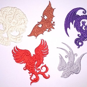 Könnte beinhalten: Fünf gestickte Bügelbilder mit einem Totenkopf, einer Fledermaus, einem Drachen, einem Phönix und einem Vogel. Die Patches sind alle weiß, braun, lila, rot und silber.
