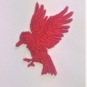 May include: A red embroidered bird with intricate details, resembling a raven or crow, with its wings spread out.