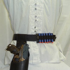 May include: A white button-down shirt with decorative buttons, a black belt with a holster and toy gun, and a belt with blue and orange toy bullets. The outfit is designed for cosplay or costume events.