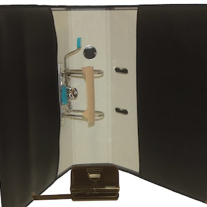 May include: Black leather binder with a metal ring mechanism and a built-in hole punch. The binder is open and the inside is white with a brown paper insert.