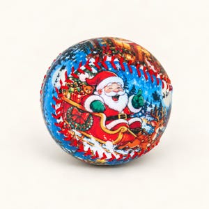 Könnte beinhalten: Ein Baseball mit festlichem Weihnachtsmotiv, das den Weihnachtsmann in einem von Rentieren gezogenen Schlitten vor einem blauen, verschneiten Hintergrund zeigt. Der Ball hat leuchtend rote Nähte entlang der Verbindungsstellen.