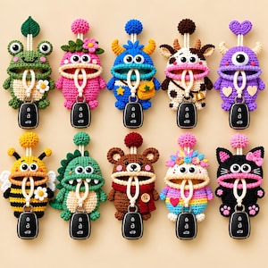 May include: Ten crocheted key pouches shaped like various creatures including a frog, monster, cow, bee, dinosaur, bear, and cat. Each pouch features a wide mouth opening, a top pom-pom, and a white cord loop holding a black car key fob.