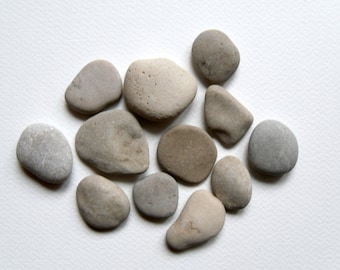May include: A collection of smooth, gray and brown stones of various sizes and shapes, arranged on a white background.