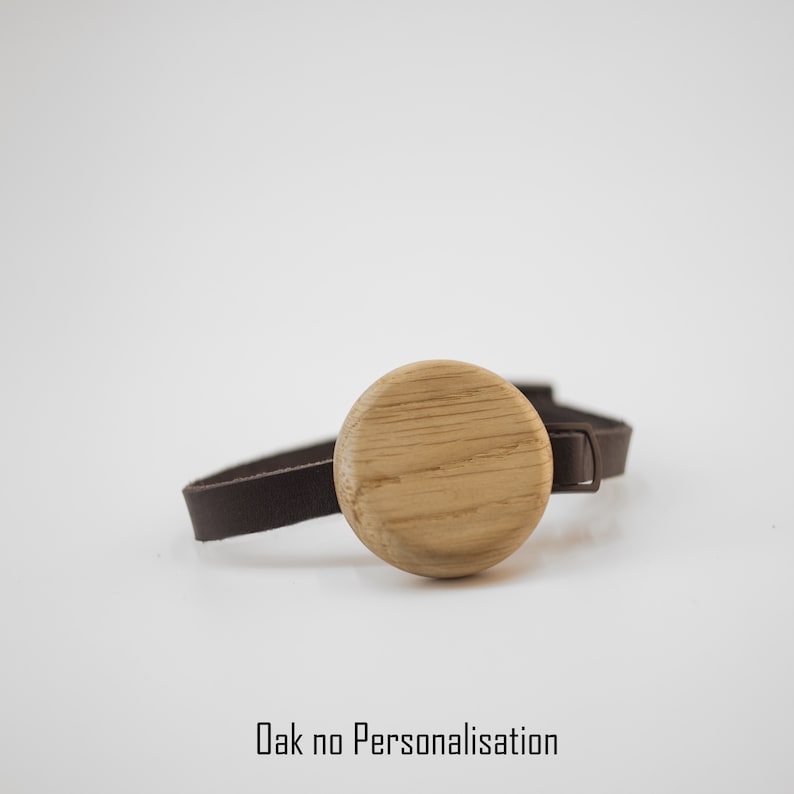 K&ouml;nnte beinhalten: Ein Eichenarmband mit einem kreisf&ouml;rmigen Mittelst&uuml;ck aus Holz und einem dunkelbraunen Lederband. Der Text "Oak no Personalisation" ist unten sichtbar. Das Armband wird vor einem wei&szlig;en Hintergrund pr&auml;sentiert. Das Eichenmittelst&uuml;ck hat einen Durchmesser von ca. 3 cm.