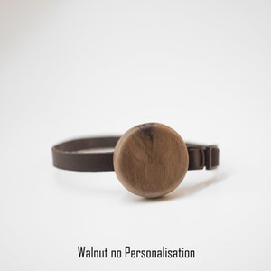 K&ouml;nnte beinhalten: Ein braunes Lederarmband mit einem runden Mittelst&uuml;ck aus Walnussholz. Das Armband hat einen Schnallenverschluss. Der Text "Walnut no Personalisation" befindet sich unten im Bild.
