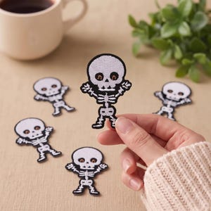 May include: Five embroidered skeleton patches featuring white skulls and rib cages with black outlines and brown eye details. Each patch depicts a cartoon-style skeleton with arms raised in a waving motion, crafted with detailed thread work.