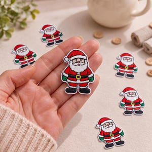 May include: A collection of embroidered Santa Claus patches featuring a red suit, white beard, black belt with a yellow buckle, green gloves, and black boots. Each patch has a white border and depicts a cartoon-style Santa figure.