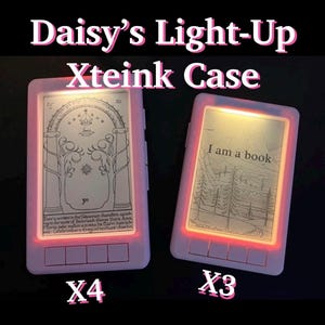 May include: Two white light-up e-reader cases with glowing red edges. The left case displays a line drawing of a gate with text below. The right case shows a landscape with trees and the text I am a book. Both feature four buttons at the bottom.
