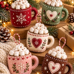 May include: Five felt mug ornaments featuring embroidered snowflake and heart designs, topped with white felt marshmallows and whipped cream. Each mug has a red and white striped hanging loop and displays intricate stitching details.