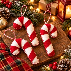 May include: Three felt candy cane ornaments featuring alternating red and white diagonal stripes. Each ornament is constructed from soft fabric with visible white stitching along the edges and includes a red and white twisted string loop for hanging.