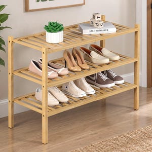 May include: A three-tier bamboo shoe rack with a slatted design. The top shelf holds a small green succulent in a white ribbed pot, a white book, and three wooden alphabet blocks. The shelves are filled with various styles of footwear.