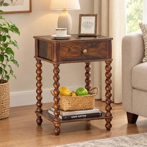 May include: A dark brown wooden side table with a single drawer featuring a round brass knob. The table has four turned spindle legs with a spherical bead design and a lower shelf holding a woven basket with fruit and two stacked books.