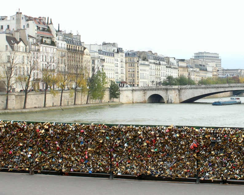 May include: A bridge over a river in Paris, France, with a wall covered in padlocks. The bridge is made of stone and has a single arch. The river is wide and calm. The wall is covered in hundreds of padlocks, all different shapes and sizes. The padlocks are a popular tourist attraction in Paris, and are said to symbolize love and commitment.