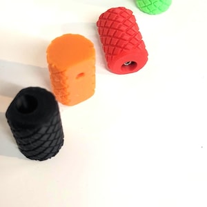 May include: Four cylindrical knobs with a textured diamond pattern on the exterior. The set includes one black, one orange, one red, and one bright green knob. Each knob features a central circular opening on the top and a small hole on the side.