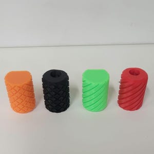 May include: Four cylindrical grips arranged in a row. The first is orange with a diamond-patterned texture, the second is black with a diamond-patterned texture, the third is light green with diagonal grooves, and the fourth is red with diagonal grooves.