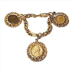 May include: Gold chain bracelet with three gold coin charms. Each coin charm is surrounded by a heart-shaped design.
