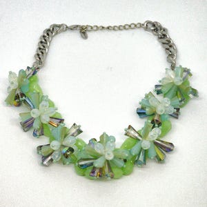 May include: A green and white beaded necklace with a silver chain. The beads are arranged in a floral pattern.
