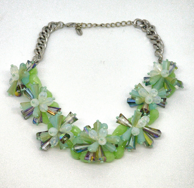 May include: A green and white beaded necklace with a silver chain. The beads are arranged in a floral pattern.