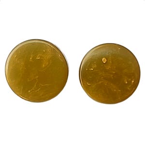 May include: Two round, golden-yellow earrings with a marbled effect. The earrings have a glossy finish and a simple, minimalist design. The earrings are a solid color with a slight variation in tone.
