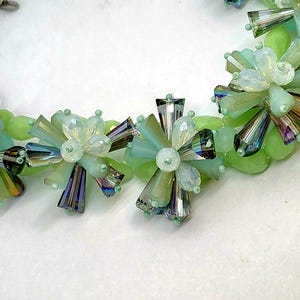 May include: A green and iridescent crystal beaded necklace with a silver chain. The beads are arranged in a flower shape.