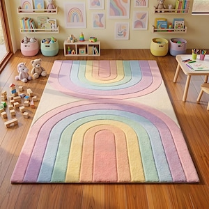 May include: A rectangular area rug featuring a symmetrical rainbow pattern with concentric arches in pastel shades of pink, yellow, blue, and purple on a cream background. The rug has a textured, tufted surface and is placed on a wooden floor.