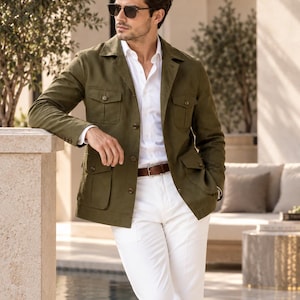 Peut inclure: Une veste utilitaire vert olive dotée de quatre poches à rabat sur le devant avec fermetures à boutons, portée sur une chemise blanche à boutons et un pantalon blanc avec une ceinture en cuir marron. La veste présente un col et des manches longues.