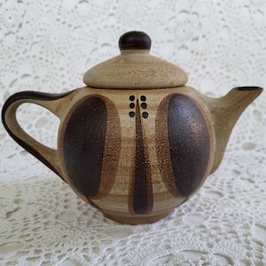 May include: A brown and tan ceramic teapot with a geometric design. The teapot has a lid and a spout.