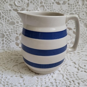 May include: A ceramic pitcher with a white base and horizontal blue stripes. The pitcher has a handle and a spout for pouring. The design is simple and classic, suitable for serving beverages.