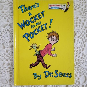 May include: A yellow book cover with the title "There's a WOCKET in my POCKET!" by Dr. Seuss. The book is part of the "Bright and Early Books for Beginning Beginners" series. The cover features an illustration of a boy with a green creature sticking out of his back pocket.