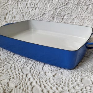 May include: A rectangular, blue enamel baking dish with a white interior. The dish has curved handles on each end. The exterior is a vibrant blue, and the interior is white. This vintage cookware is perfect for baking.