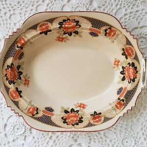 May include: A white oval serving dish with a gold rim and floral pattern. The dish has a scalloped edge and two gold handles.