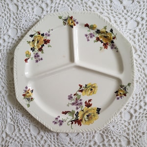 May include: A white divided serving plate with a floral design featuring yellow, purple, and red flowers. The plate has three sections.