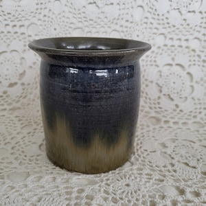 May include: A dark blue and brown ceramic vase with a textured glaze. The vase is sitting on a white crocheted doily.