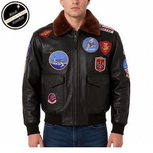 May include: A black leather bomber jacket featuring a brown faux fur collar, a front zip fastening, and two flap pockets. The jacket is decorated with various colourful embroidered military-style patches on the chest and sleeves, including a ship graphic.