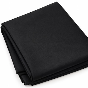 Peut inclure: Un tissu noir uni plié en une pile rectangulaire soignée. Le matériau présente une finition mate cohérente et une texture lisse et uniforme sur toute la surface, avec des bords nets et des plis précis et marqués sur le côté.