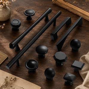 May include: A collection of matte black cabinet hardware including long cylindrical bar pulls, arched handles, and various knob shapes such as round, octagonal, and square designs. These metal fixtures feature a smooth finish and solid construction.