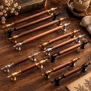 May include: A collection of drawer pulls featuring cylindrical wooden handles paired with metal mounting hardware. The hardware comes in various finishes including brushed gold, polished silver, and matte black, each with decorative end caps.