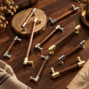 Peut inclure: Une collection de poignées de placard composées de cylindres en bois brun foncé associés à des embouts métalliques aux finitions argent poli ou or brossé. Chaque poignée est dotée de deux points de fixation pour meubles ou armoires.