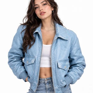 Puede incluir: Una chaqueta tipo bomber de color azul claro con acabado desgastado, que presenta un cuello clásico, una cremallera metálica plateada completa y dos bolsillos delanteros con solapa y botones de presión plateados. Puños y dobladillo acanalados.