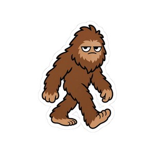 May include: A die-cut sticker featuring a cartoon illustration of a brown, furry Bigfoot creature walking. The creature has a thick coat of brown fur, lighter brown hands and feet, and a grumpy facial expression with heavy eyelids and a frown.